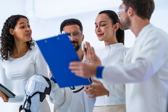 Robotics user testing debrief: an analyst holds up her blue clipboard as three colleagues in white compare the test sheet beside a white humanoid robot bust on its plinth