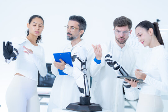 Bionic engineering workshop: a developer brings both palms around the dark gripper of a lab robot while a woman in a mechanical arm turns her face toward the camera