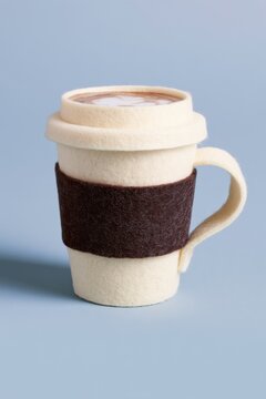 Handmade felt coffee cup features a soft ivory body, dark brown sleeve, and curved handle, positioned against a light blue backdrop for visual appeal
