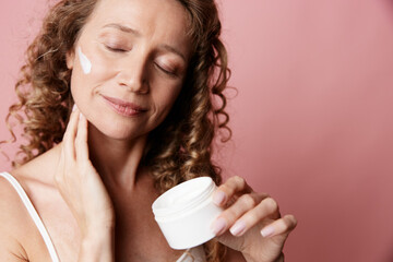An authentic middle aged woman applies cream to her face, showing natural skin without retouching....