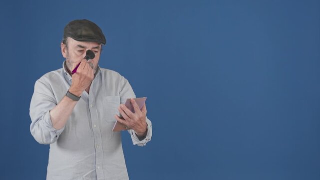 Mature male actor applying makeup powder with brush before audition