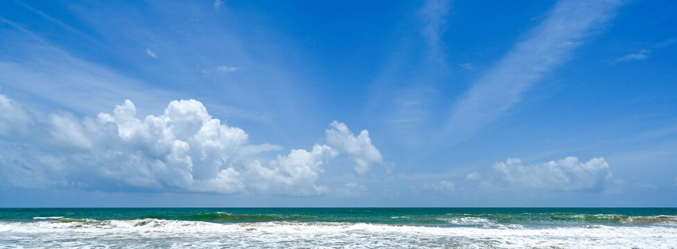 Vast ocean horizon under a bright blue sky with fluffy white clouds and gentle waves