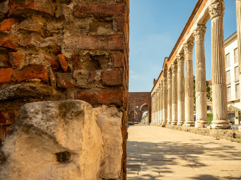 an ancient red-brick wall in the foreground, with the ancient Roman colonnade of San Lorenzo in Milan in the background