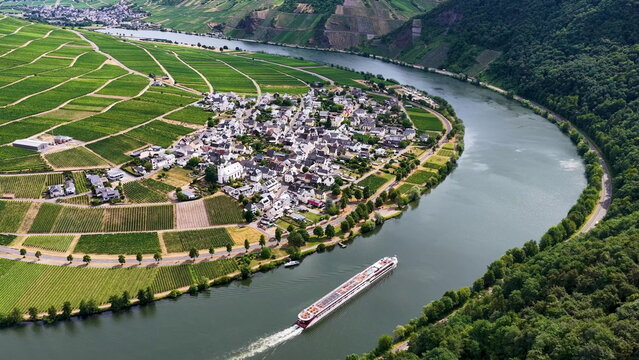 Luftaufnahme der malerischen Moselschleife bei Minheim mit einem eleganten Flusskreuzfahrtschiff auf dem Wasser, umgeben von gr&uuml;nen Weinbergen im Sommer.