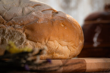 A rustic round loaf of bread sits on a wooden board in dim lighting. Concept of artisanal baking, homemade food, and traditional culinary arts. © kinomaster