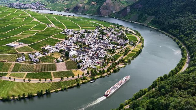 Luftaufnahme der malerischen Moselschleife bei Minheim mit einem eleganten Flusskreuzfahrtschiff auf dem Wasser, umgeben von gr&uuml;nen Weinbergen im Sommer.