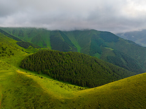 Scenic panorama features rolling green mountains and dense coniferous forest. Dramatic cloud formations create a serene atmosphere over the landscape.