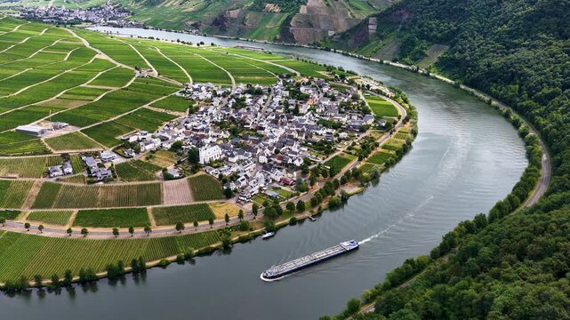 Luftaufnahme der Moselschleife bei Minheim mit einem langen Binnenschiff auf dem Fluss, umgeben von gr&uuml;nen Weinbergen und einem Weindorf im Sommer.