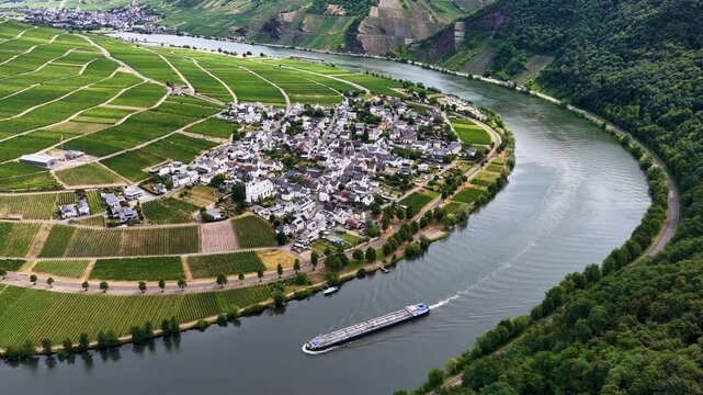 Luftaufnahme der Moselschleife bei Minheim mit einem langen Binnenschiff auf dem Fluss, umgeben von gr&uuml;nen Weinbergen und einem Weindorf im Sommer.