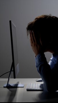 Overworked person experiencing severe stress and burnout, sitting in front of a computer screen with hands covering face, indicating frustration, anxiety, and mental exhaustion from demanding work