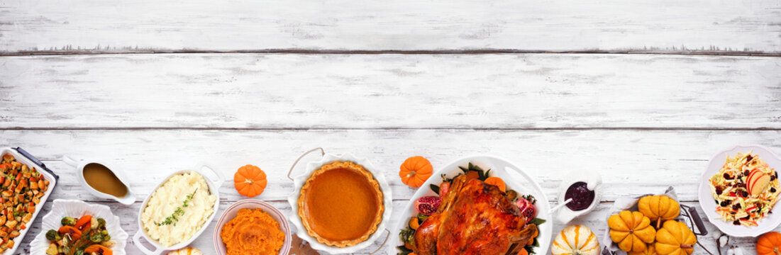 Thanksgiving turkey dinner. Top view bottom border on a rustic white wood table banner background. Turkey, mashed potatoes, stuffing, pumpkin pie and sides.