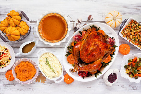 Thanksgiving turkey dinner. Overhead view table scene on a rustic white wood table background. Turkey, mashed potatoes, stuffing, pumpkin pie and sides.