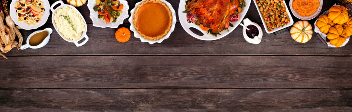 Thanksgiving turkey dinner. Above view top border on a rustic dark wood table banner background. Turkey, mashed potatoes, stuffing, pumpkin pie and sides.