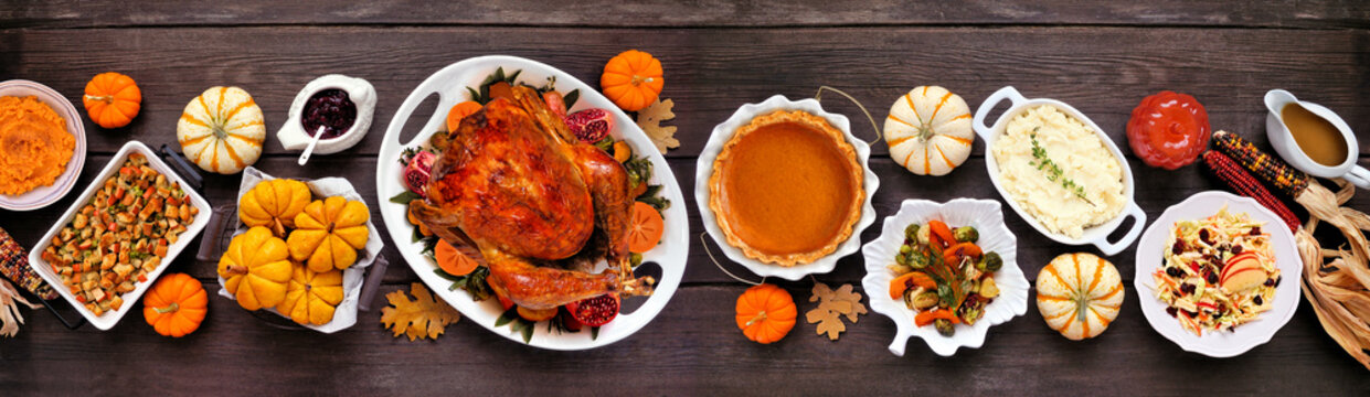 Thanksgiving turkey dinner. Top view table scene on a rustic dark wood table banner background. Turkey, mashed potatoes, stuffing, pumpkin pie and sides.