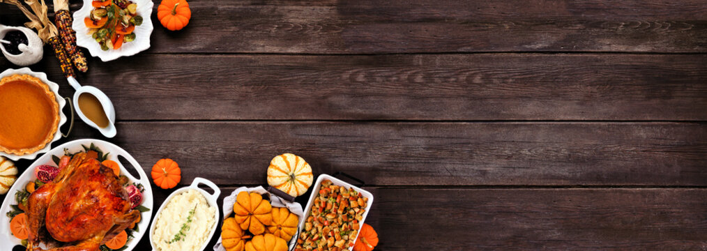 Thanksgiving turkey dinner. Overhead view corner border on a rustic dark wood table banner background. Turkey, mashed potatoes, stuffing, pumpkin pie and sides.
