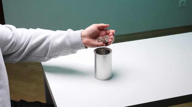 Person's hand dropping a coin into a plain metal can, symbolizing donation, charity, saving and financial contribution for future goals, fundraising and support efforts