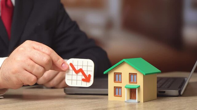 A private house and a large red downward arrow. Falling housing prices and declining property values. Real estate market downturn and economic crisis scenario.