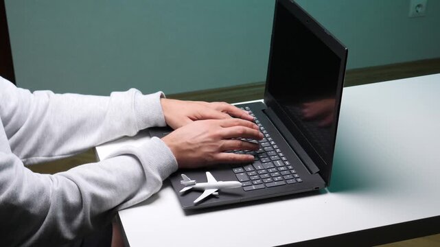 Person typing on a laptop keyboard with a small airplane toy beside it, symbolizing online travel planning, vacation booking, and digital trip arrangements