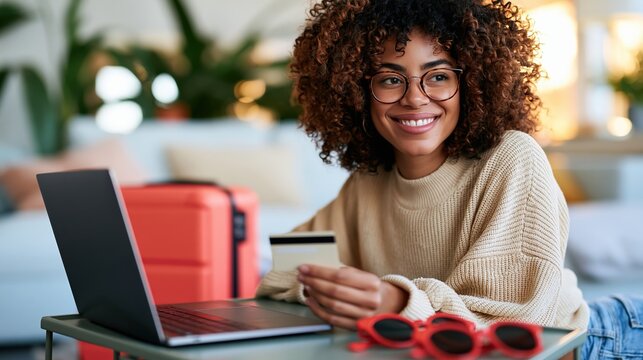 Smiling woman booking vacation online at home with laptop and payment card