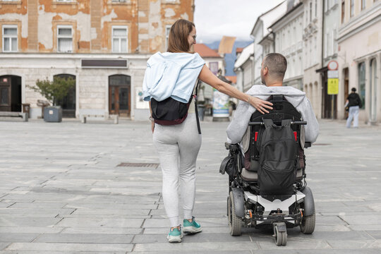 Woman personal assistant walks next to a man in a wheelchair in an urban area. They are enjoying city mobility together.