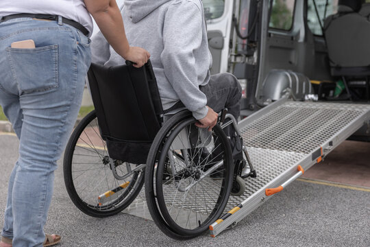 A person in a wheelchair receives help using a ramp to get into an adapted van. Personal assistant provides support in a parking area.
