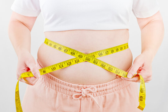 Person measures a waist with a yellow tape on a white background