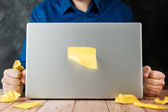 Man clenches fists beside a closed laptop with a sticky note on the lid