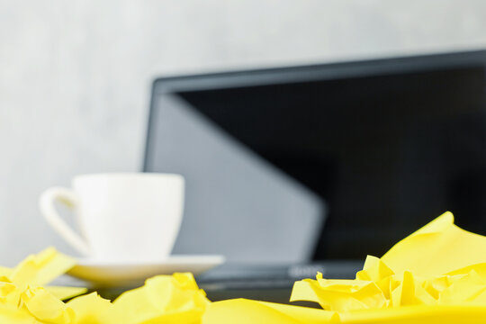 Crumpled yellow notes sit in front of a coffee cup and blurred laptop