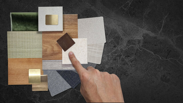 Interior Designer Hand Pointing at Material Swatch Sample Board: Wood Veneer, Tile, Fabric, Velvet, and Metal Finishes Arranged on Dark Marble Countertop for Architect Selection and Home Renovation.