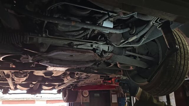 Mechanic inspects undercarriage of car in garage during daytime