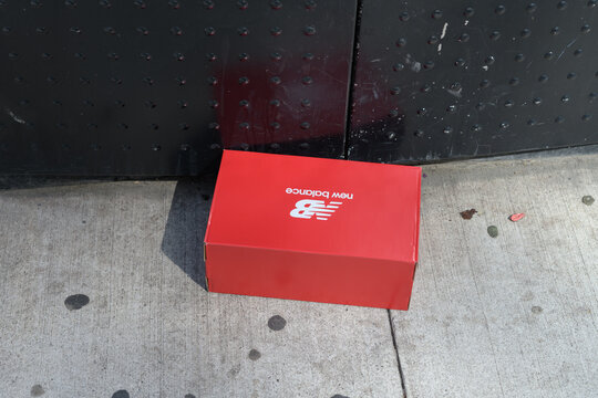 discarded NB (New Balance) footwear box on a sidewalk near a recycling bin in Toronto