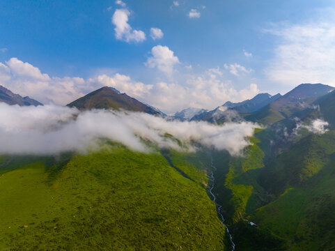 Aerial view captures vast mountain landscape with rolling green hills and winding river in Kyrgyzstan. Bright blue sky and wispy clouds enhance the serene atmosphere.