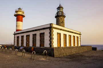Vista en ángulo del antiguo faro de piedra y el nuevo faro de rayas rojas y blancas en Fuencaliente, La Palma, a la luz del atardecer. © Maxi Perez