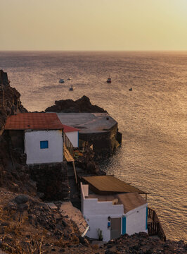 Vista vertical de casas de pescadores en el acantilado de Fuencaliente con peque&ntilde;as embarcaciones fondeadas en el mar al atardecer.