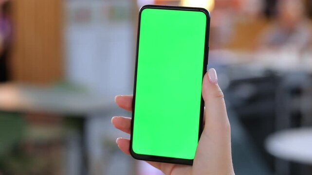 Hand holds phone with green screen. Background shows blurred cafe interior. Three keyframes show same action. Person has light skin