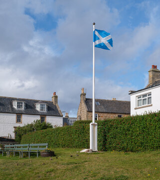 Saltire flag waving in the wind above a green grass hill at Findhorn Bay in the coastal village of Findhorn located in the region of Moray Scotland