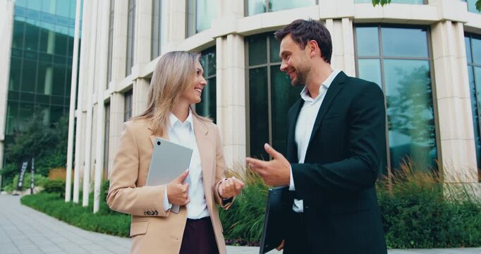 Professional business man and woman standing outdoors and looking at the camera with confident expressions, representing teamwork, corporate culture, and modern office professionals. Slow motion
