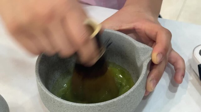 Barista whisking green matcha tea in ceramic bowl with bamboo whisk on counter for cafe and beverage banner, horizontal