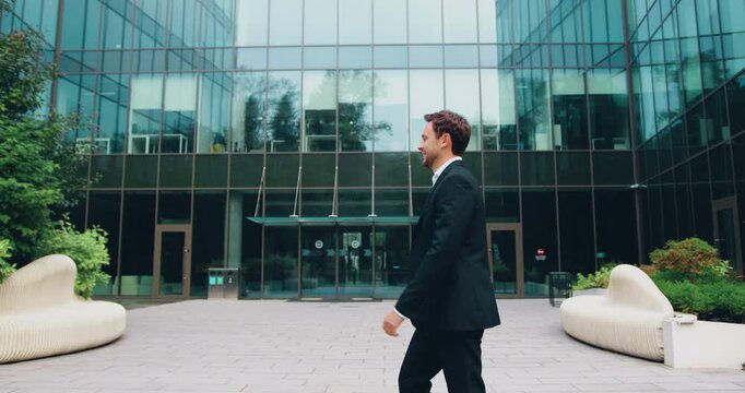 Two colleagues of adult man and young woman, walk toward each other outside a modern office building, smiling cheerfully, exchanging a high five, then parting ways to continue their day