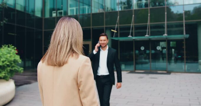 Back view of businessman and businesswoman walking together along city street near modern office building, discussing work matters. Concept of teamwork, corporate lifestyle, business communication