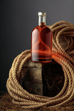 Bottle of whiskey on a rough wooden crate with hay, next to a natural hemp rope.