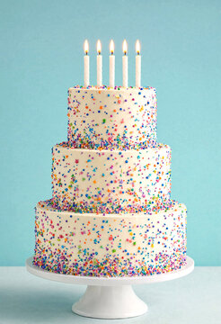 Colorful three tier birthday cake with lit candles on white stand