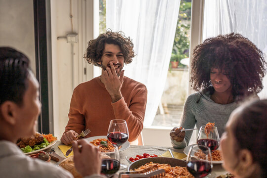 Diverse young friends enjoy a relaxed lunch together, sharing food, laughter and conversation at home. A candid multiethnic gathering conveys inclusion, friendship and belonging.