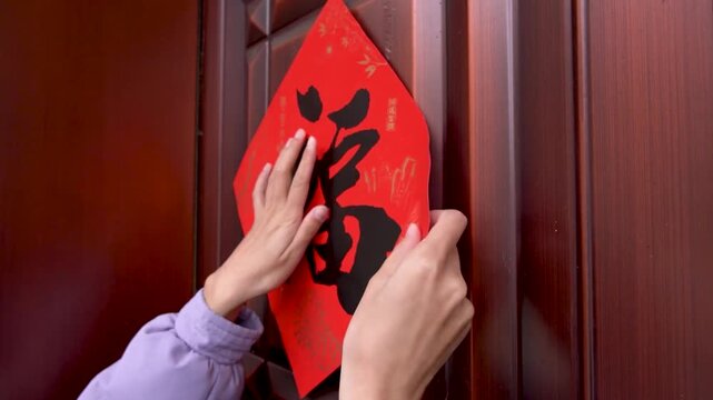Hands Placing Red Chinese Character Decoration on Wooden Door