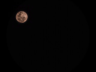 Stunning full moon glowing in a pure black night sky. Detailed lunar craters with a warm pinkish tint © MuhammadRizki