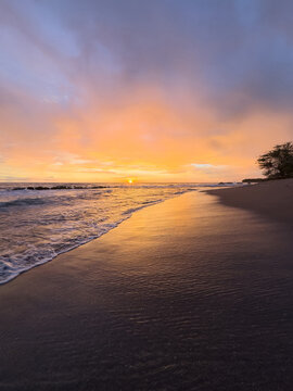 Sunset at the beach with calm waves and sandy shore