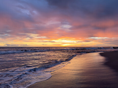 Sunset over the ocean with waves and clouds at a beach