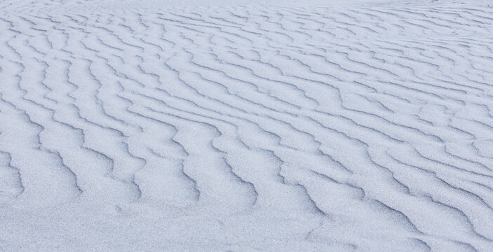 Close-up abstract of perfect wind ripple patterns in white sand dunes forming gentle waves