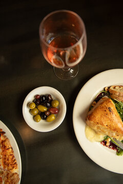 overhead shot of arugula salad with baked brie and crostini and side of olives and glass of wine