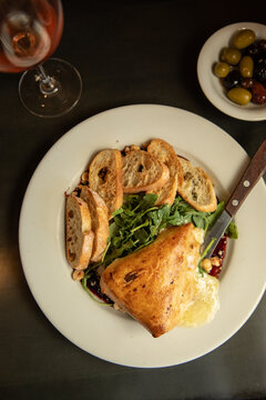 overhead shot of arugula salad with baked brie and crostini and side of olives and glass of wine